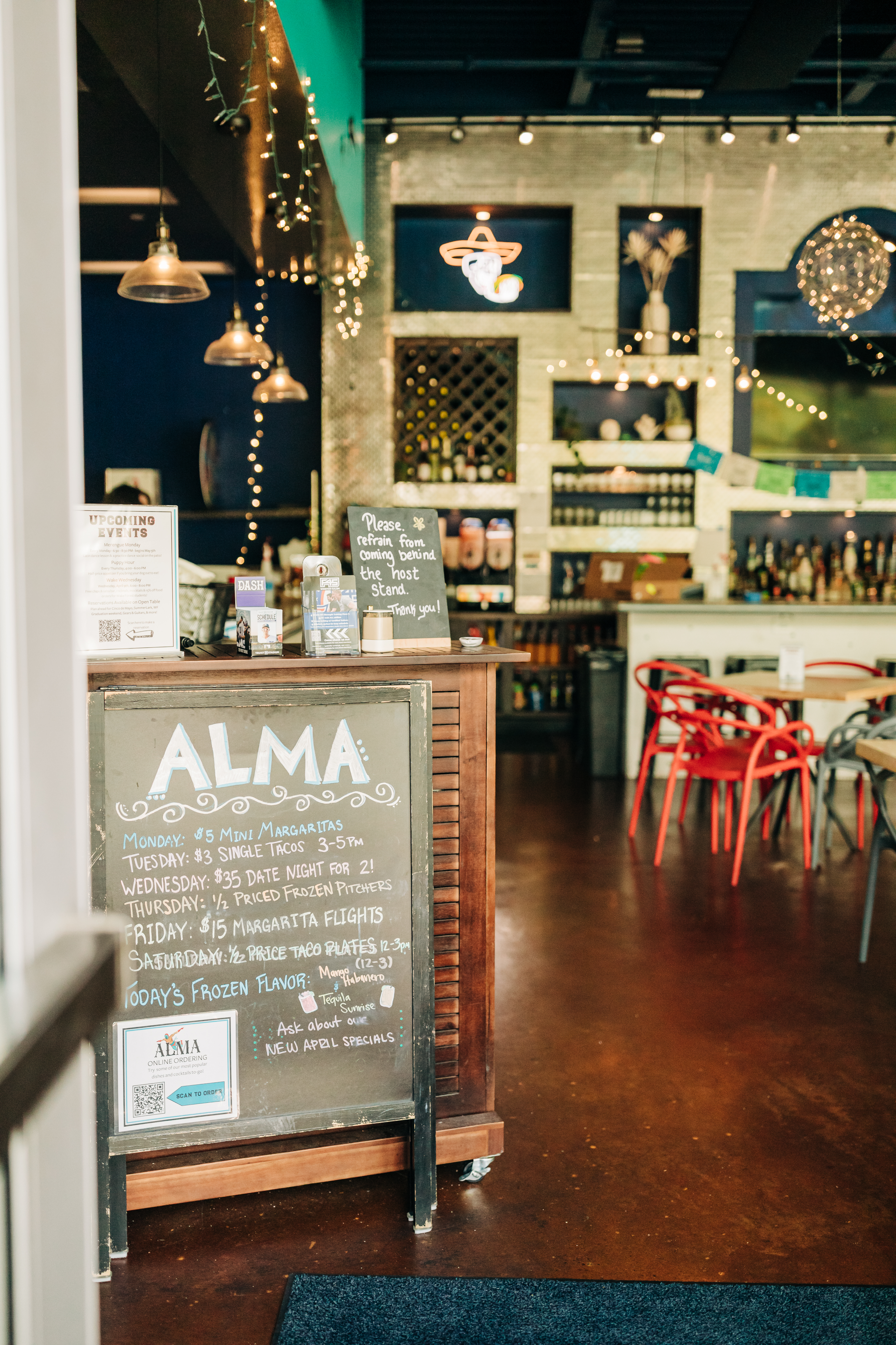 Alma restaurant interior with weekly specials chalkboard, margarita deals, and bar seating under string lights.